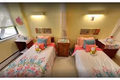 Bright bedroom with two twin beds featuring floral bedding separated by a central nightstand and wall-mounted lights.