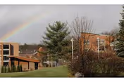 Outdoor view of a senior living facility with buildings, trees, and a rainbow in the sky.