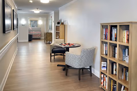 Well-lit interior hallway with a small game table and chairs, bookshelves, and seating.