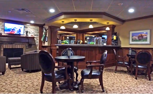 Comfortable common lounge with round tables and chairs, a fireplace, and a wooden service counter under pendant lights.