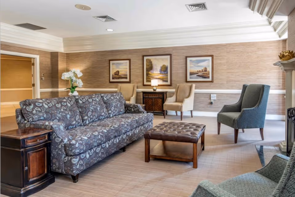 Comfortable lounge with a patterned sofa, armchairs, a tufted ottoman, side tables, and framed landscape paintings on textured walls.