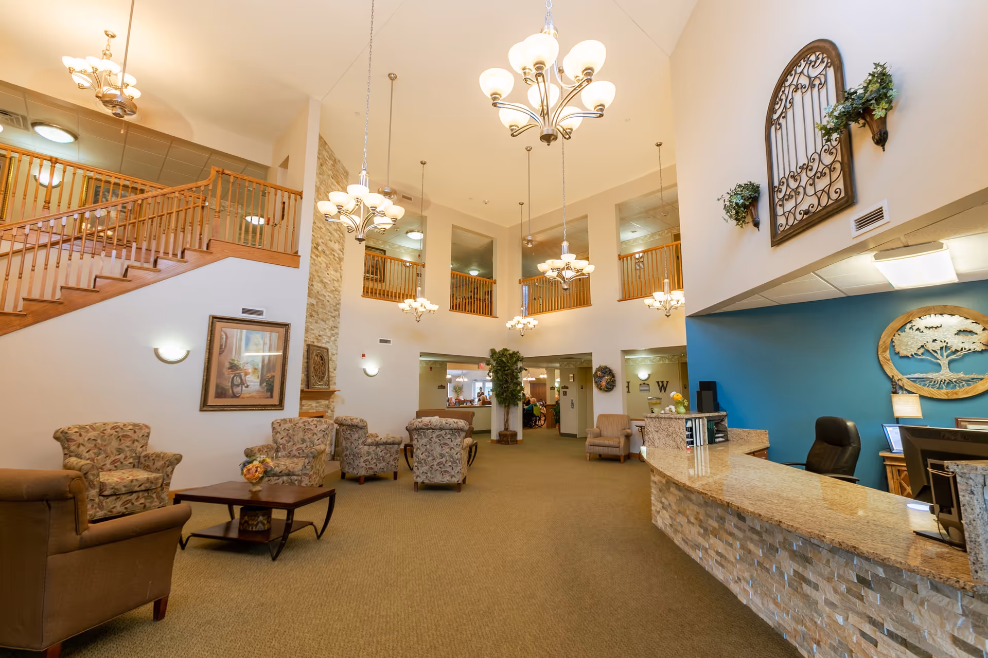 Spacious two-story reception lobby with seating area, chandeliers, a staircase and a front desk.
