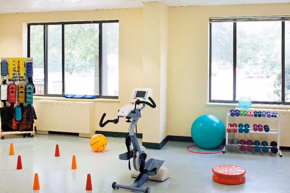 Small exercise room with a stationary bike, exercise balls, dumbbells, and cones in front of large windows.