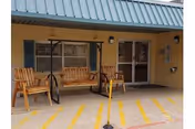 Front entrance of a nursing facility with a covered porch, two wooden swing benches, and glass double doors.