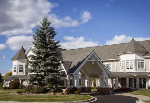 Sunrise of Troy senior living facility exterior with a driveway, trees, and a blue sky.