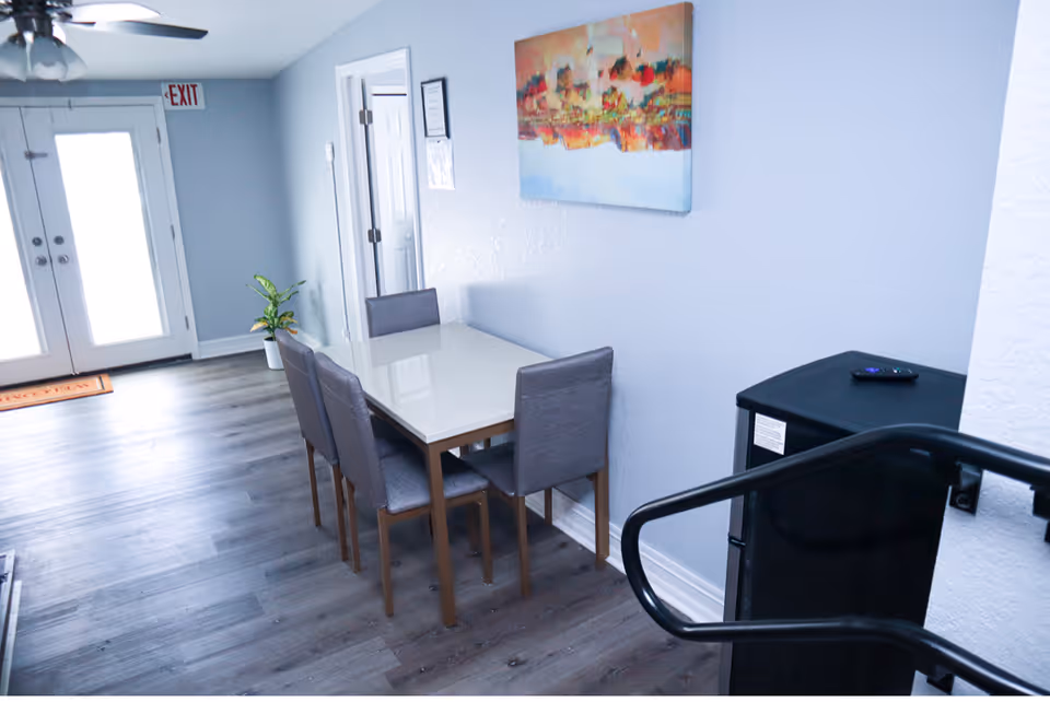 Small dining area with a table and four chairs in a bright entry foyer with double doors and wall artwork.