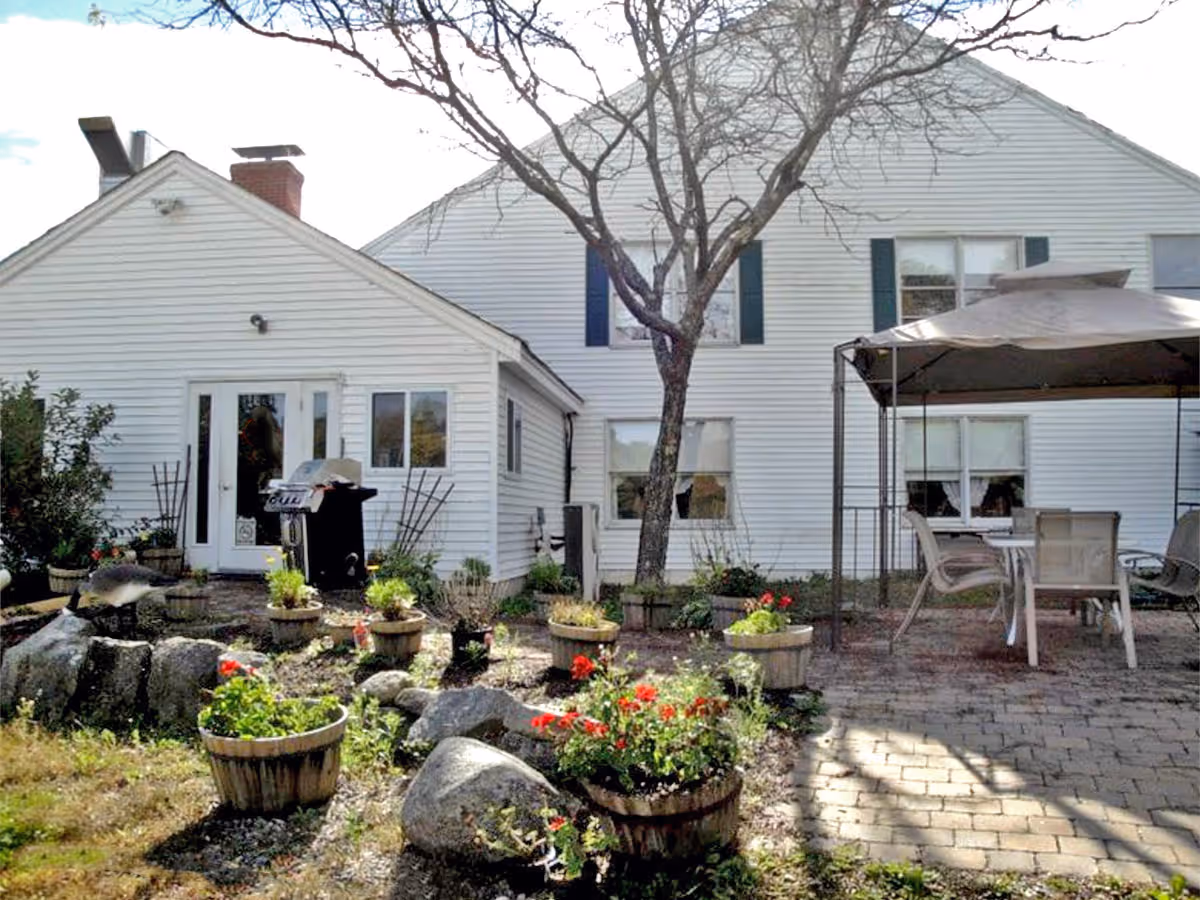 White two-story house exterior with a patio area, potted flowers, a canopy and outdoor furniture.