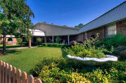 Exterior view of Leakesville Rehabilitation and Nursing Center with manicured lawn and garden beds.