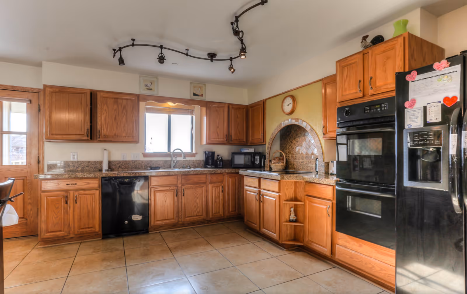 Wood-toned kitchen with granite countertops, modern appliances, and a tiled floor.