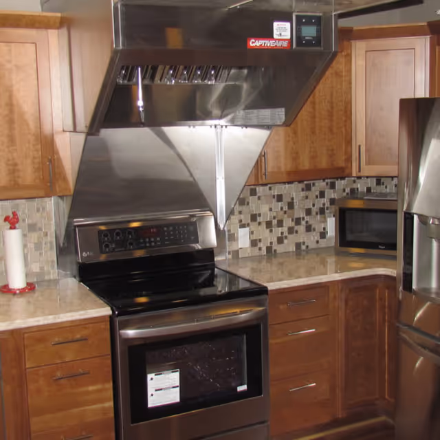 Modern kitchen with wooden cabinets, a stainless steel stove and oven, a stainless steel range hood labeled CaptiveAire, a microwave on the countertop, and a stainless steel refrigerator.