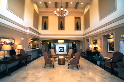 Spacious, elegant senior living facility lobby with seating arranged around a central fireplace under a chandelier.