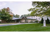 Single-story senior living facility with a covered entrance, manicured lawn, and trees.