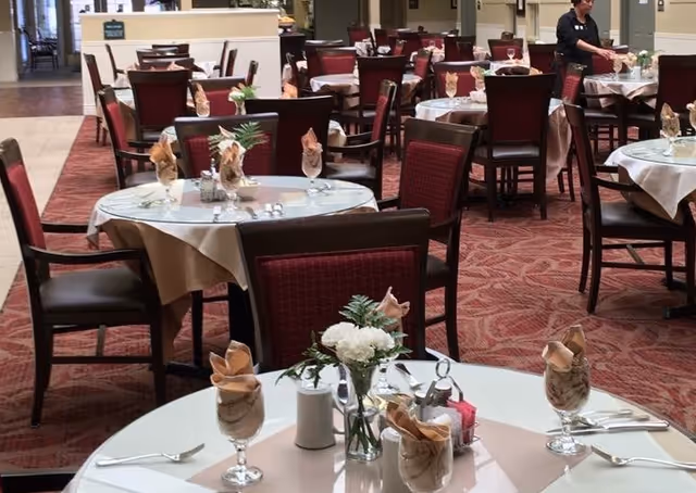 Dining room with multiple round tables set with napkins, glassware, and floral centerpieces.