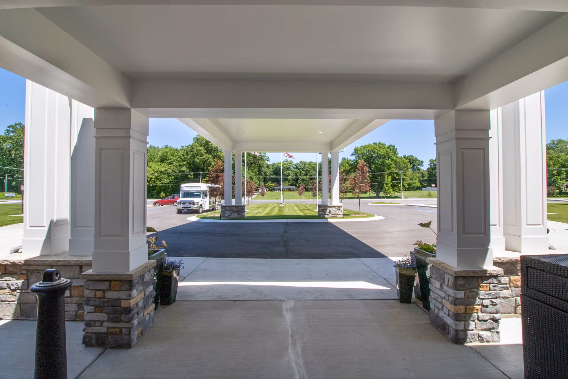 Covered front entrance with white columns and stone bases overlooking a circular driveway, landscaping, and a flagpole.