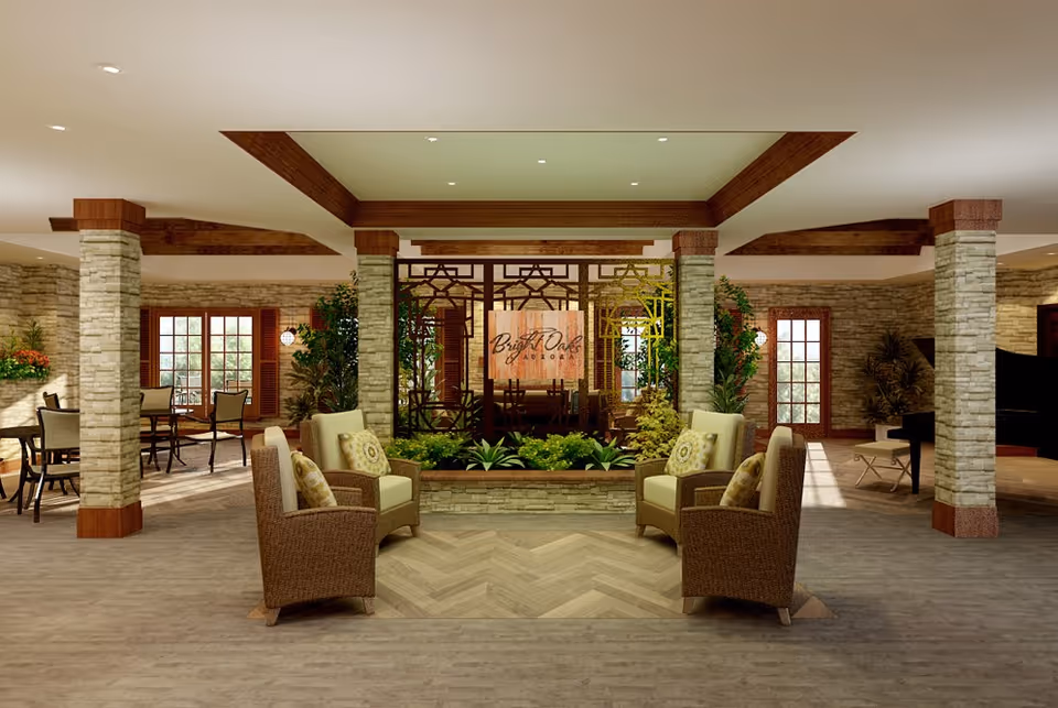 A spacious and well-lit common area with stone pillars and wooden beams on the ceiling. The room features comfortable wicker armchairs with cushions arranged around a central planter filled with greenery. In the background, there are tables and chairs near large windows with wooden shutters, and a grand piano is visible on the right side. The walls are made of stone, and the floor has a wood-like finish. A decorative wooden screen with the text 'Bright Oak' is seen in the center background.