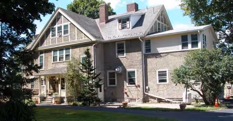 Exterior view of a two-story senior living facility with a manicured lawn and trees.