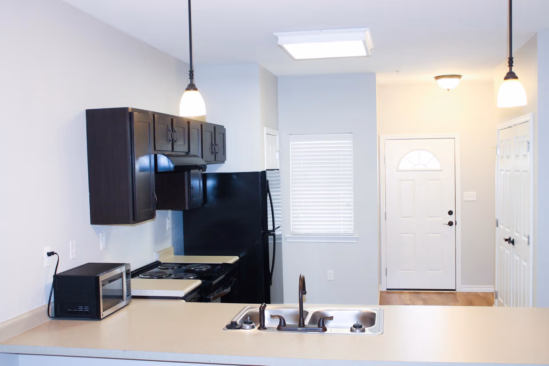 Open kitchen featuring a countertop with sink, dark upper cabinets, stove and refrigerator, with the entry door visible beyond.