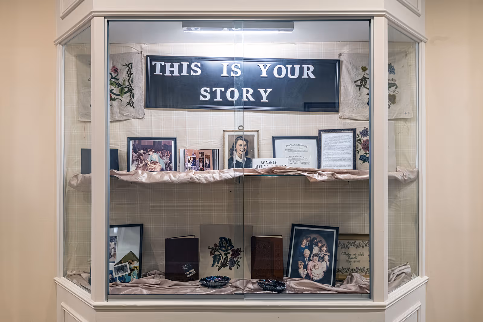 Glass display case holding photos, books and memorabilia with a banner reading "THIS IS YOUR STORY".