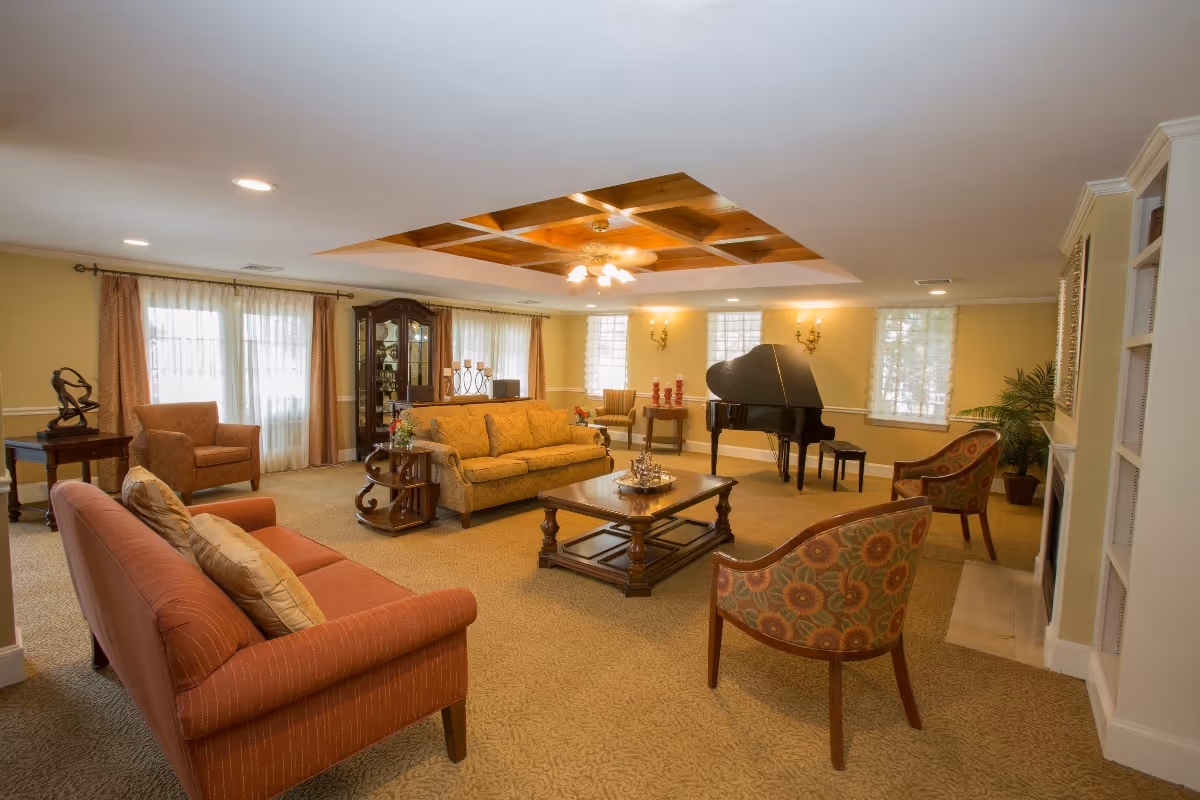 Spacious communal living room with sofas, armchairs, a coffee table and a grand piano under decorative ceiling paneling.