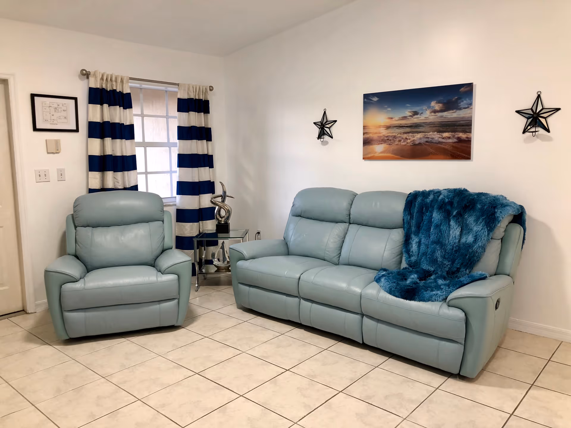 Light teal leather living room with loveseat, chair, striped curtains, beach print, and star accents.