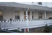 Front porch of a white building with string lights and railing.