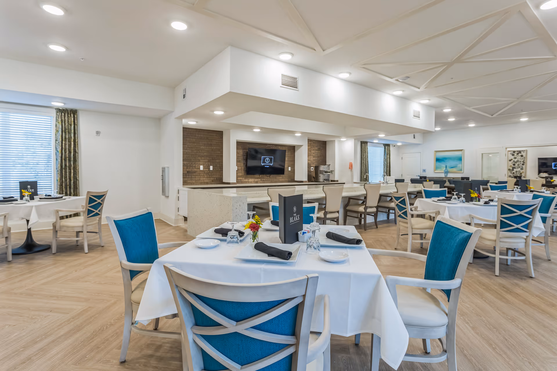 Spacious dining room with white-tablecloth tables, teal-cushioned chairs, and a central serving area.