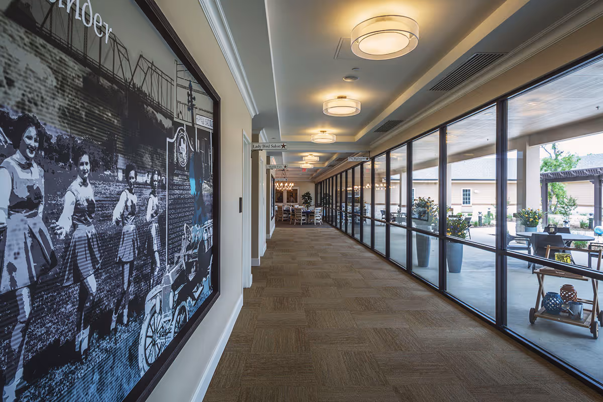 Long carpeted interior corridor with a large historic mural on the left and floor-to-ceiling windows revealing a patio on the right.