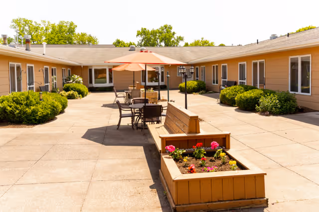 Sunny central courtyard with planter boxes, benches and umbrella-shaded tables surrounded by single-story residential wings.