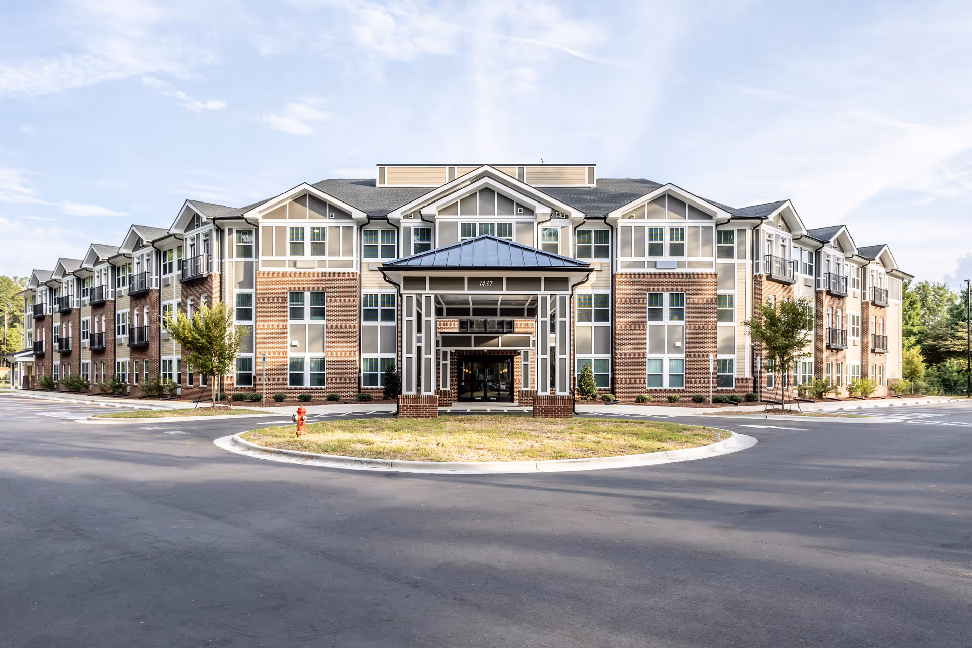 Front view of a three-story brick and siding senior living building with a covered entrance and circular driveway under a blue sky.