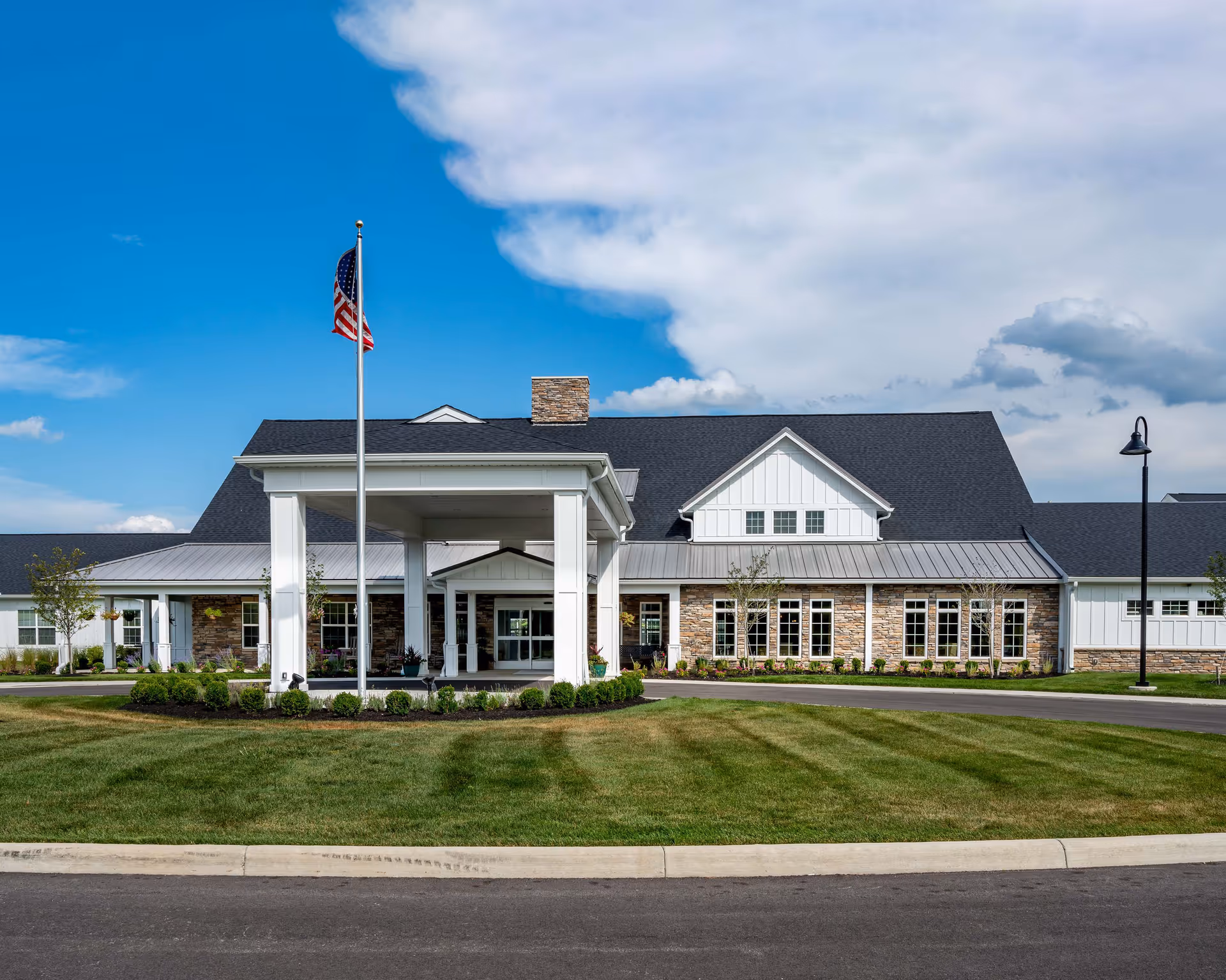 Front exterior of the Walnut Crossing senior living building with a covered entrance, flagpole, and manicured lawn.