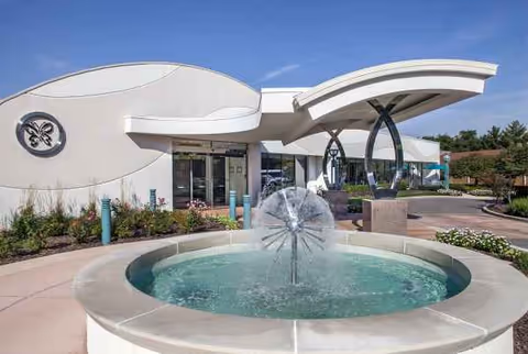 Modern Delmar Gardens on the Green exterior with a circular fountain in front.
