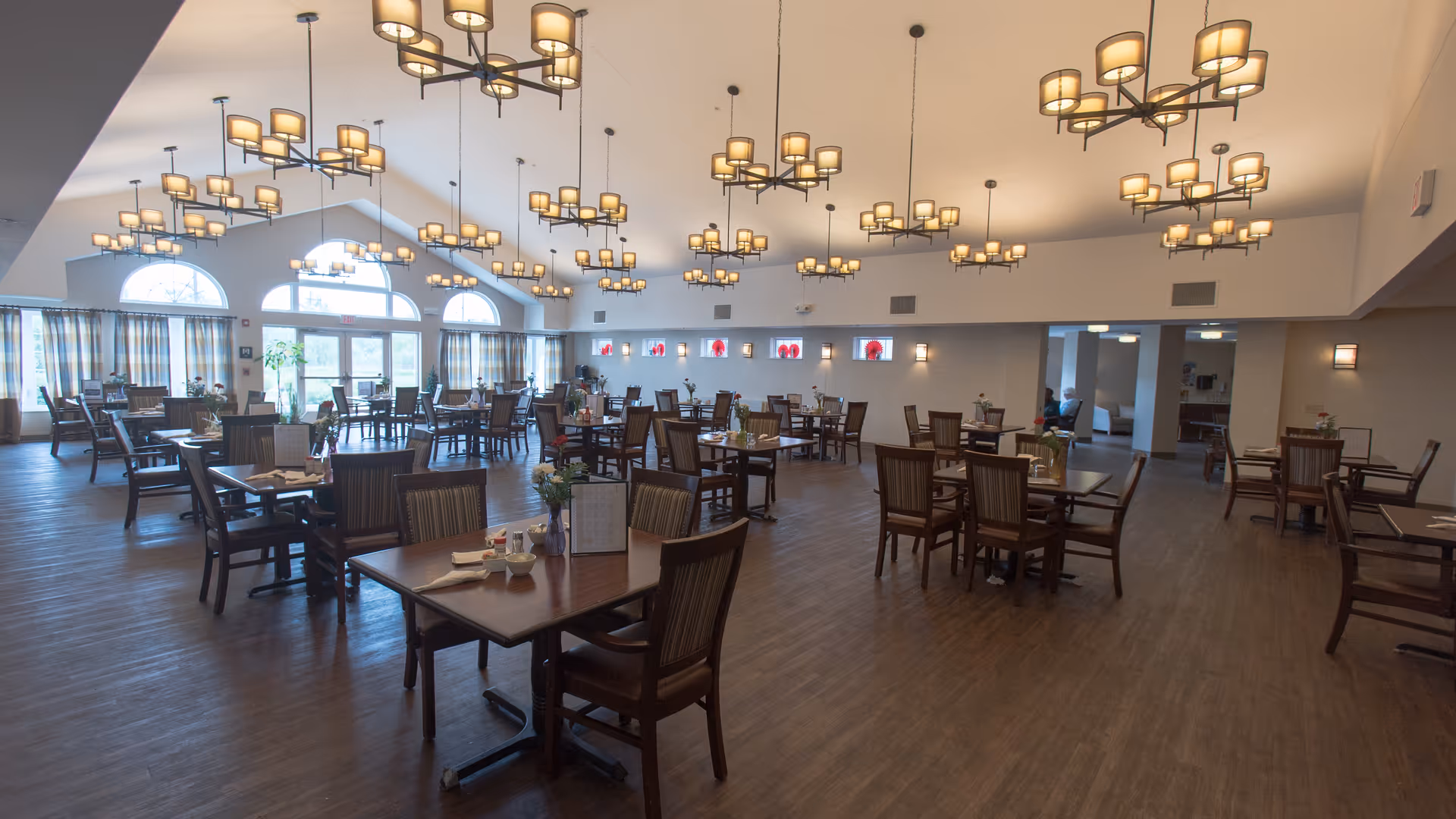Spacious dining room with multiple wooden tables and chairs and hanging chandeliers.