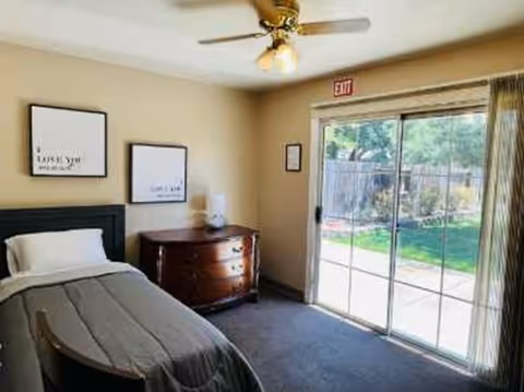 A bedroom in a senior living facility with a bed, dresser, and glass door.