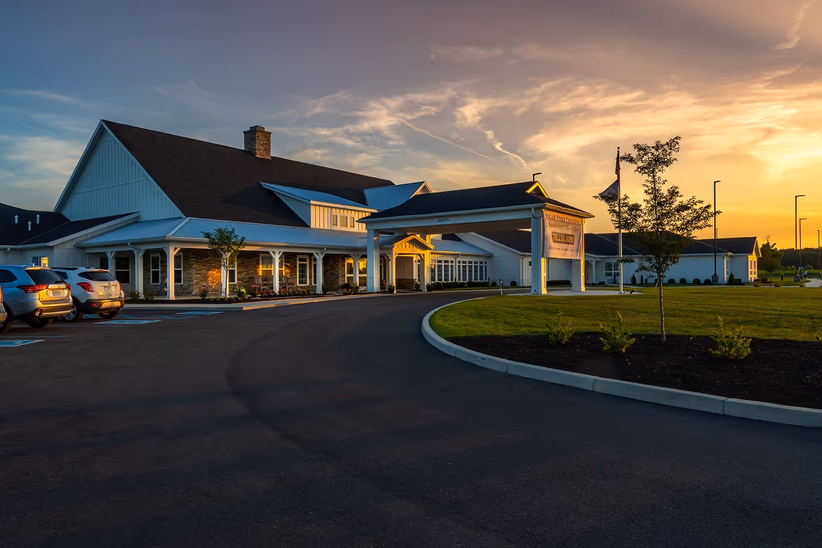 Senior living facility front entrance at sunset with parked cars and landscaped lawn.