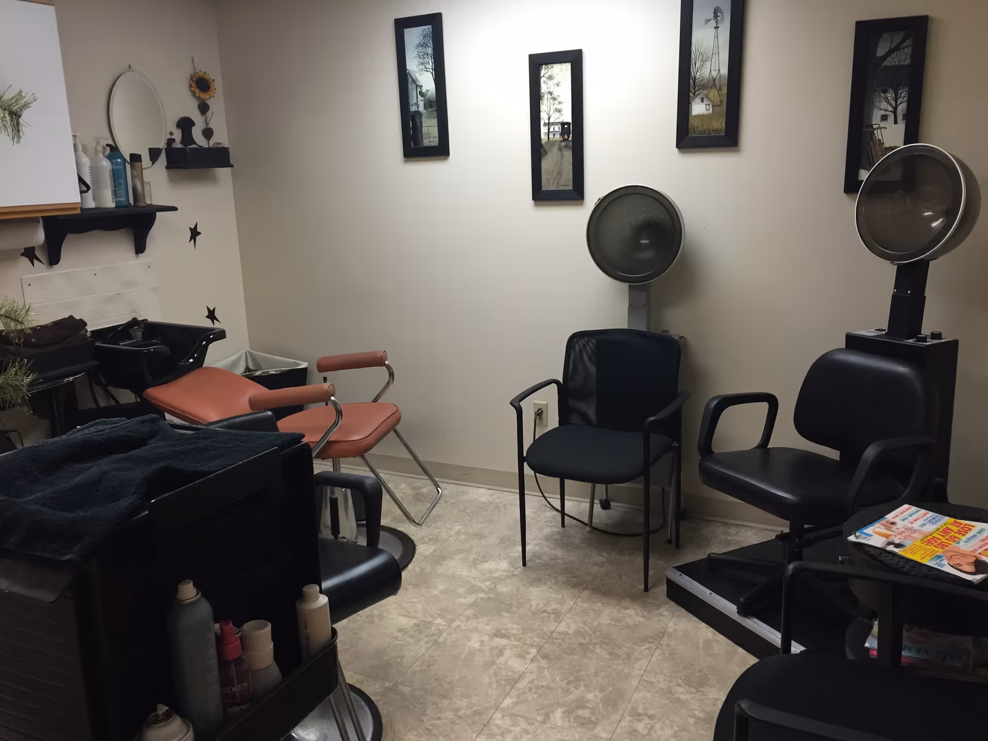 Small salon room with multiple styling chairs, hooded hair dryers, a shampoo sink and a cart of hair products.