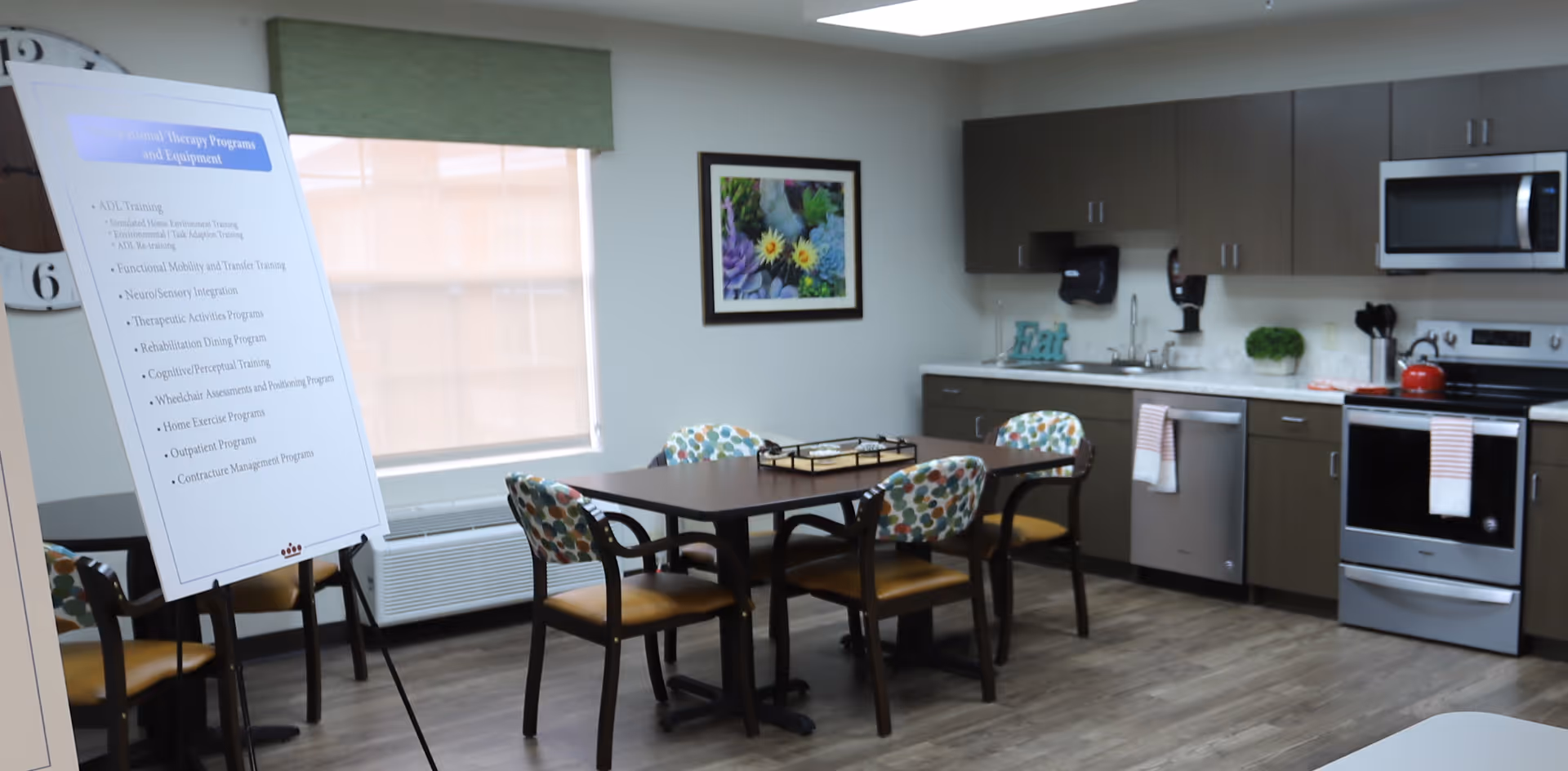 Communal dining and kitchenette area with a table and chairs, modern appliances, and an informational easel.