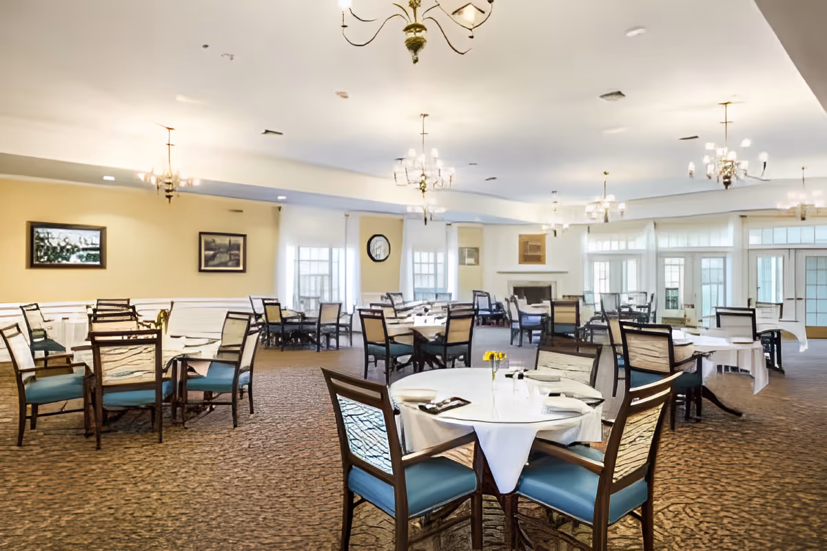 Spacious dining room with round tables set with white tablecloths and chairs beneath chandeliers.
