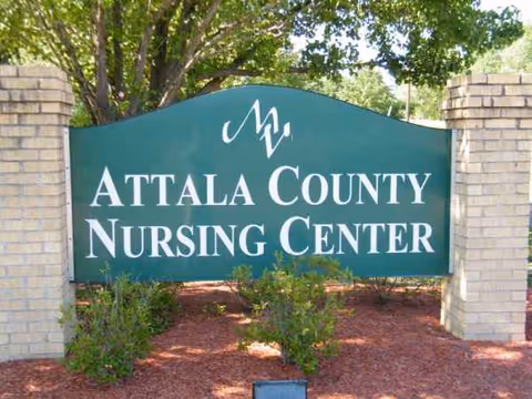 A green Attala County Nursing Center sign stands between brick pillars at a landscaped entrance.