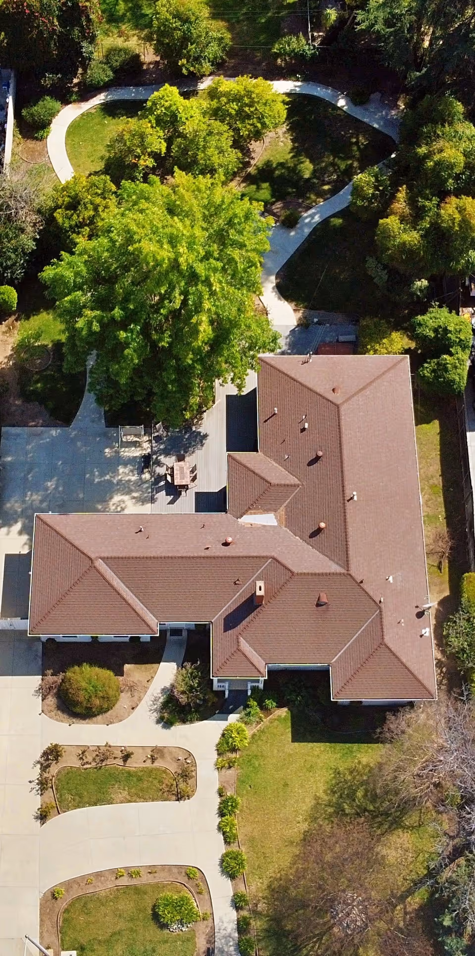 Aerial view of a single-story senior living building with a red roof surrounded by walkways, lawns, and trees.