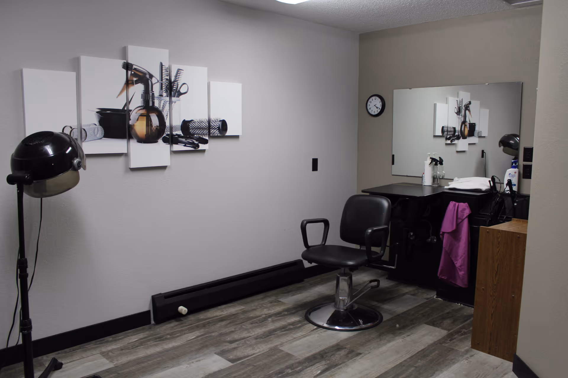 Small hair salon/styling room with a salon chair, wall mirror, hooded dryer, counter and hair-care items.