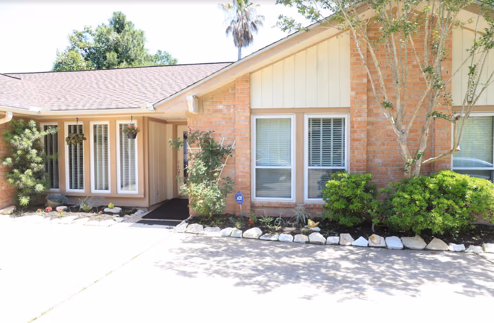 Front exterior of a single-story brick building with windows, an entry walkway, and landscaped shrubs and hanging plants.
