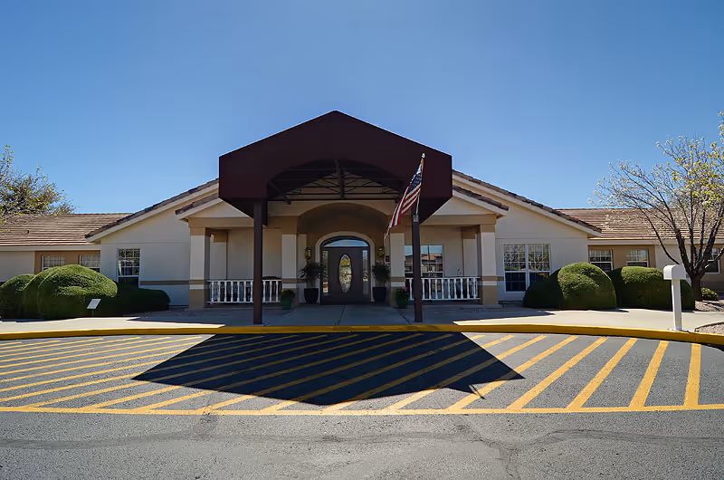 Front entrance of Brookdale East Mesa with a covered porte-cochère, an American flag, and neatly trimmed shrubs.