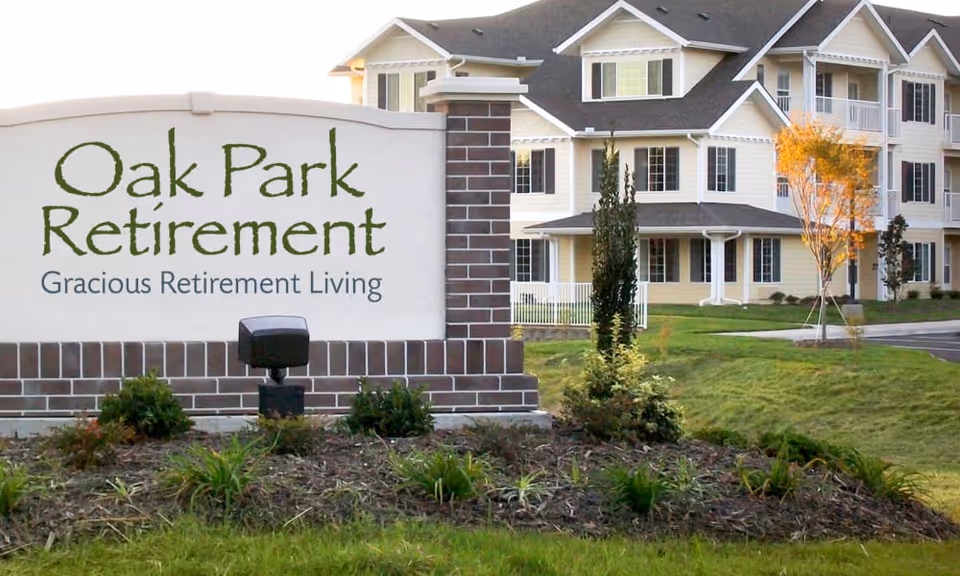 Outdoor view of the entrance sign for Oak Park Retirement with the tagline 'Gracious Retirement Living' in front of a multi-story residential building surrounded by landscaped greenery.