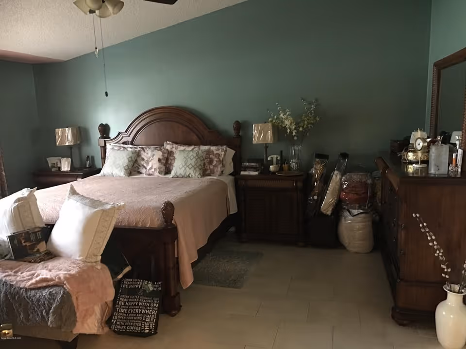 Bedroom with a wooden bed, nightstands, dresser and decorative pillows against a teal-green wall.