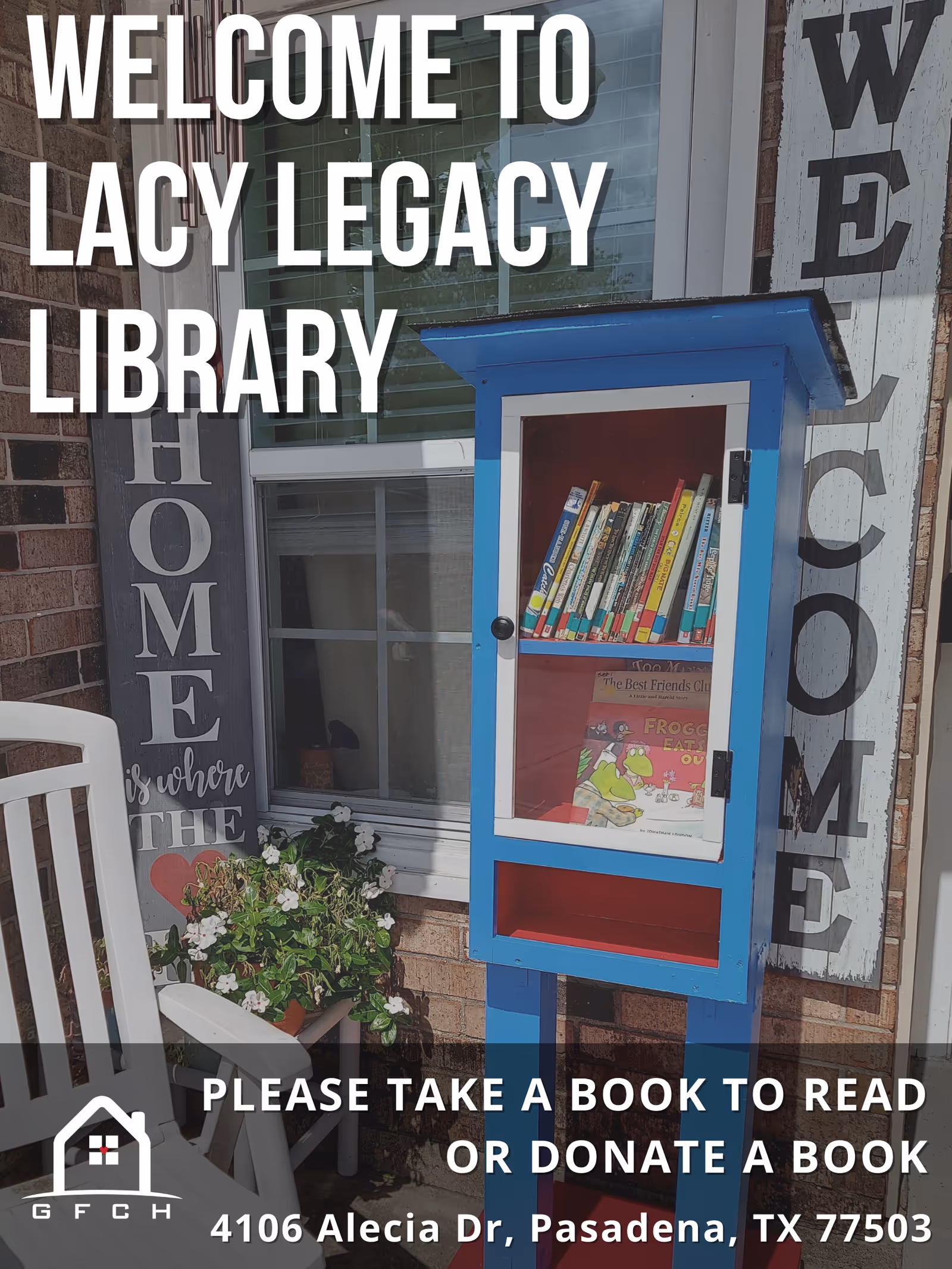 A small blue free library box on a porch against a brick wall with welcome signs, plants, and a chair.