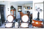 Interior view of a formal dining room with two upholstered chairs in the foreground, a dining table with chandelier, and a china cabinet and decorative furnishings.