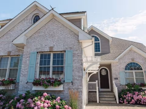Front exterior of a brick senior living building with blue shutters and blooming flowers.