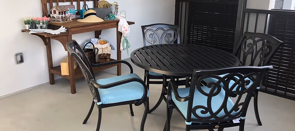 Round black metal patio table with four matching chairs with light blue cushions beside a wooden console table holding hats and decorative items.