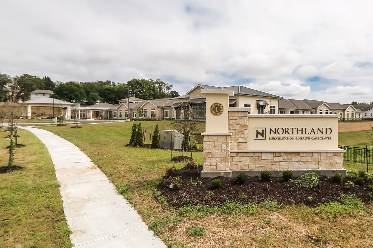 Stone entrance sign for Northland Rehabilitation & Health Care Center in front of the facility with a curved sidewalk and landscaped lawn.
