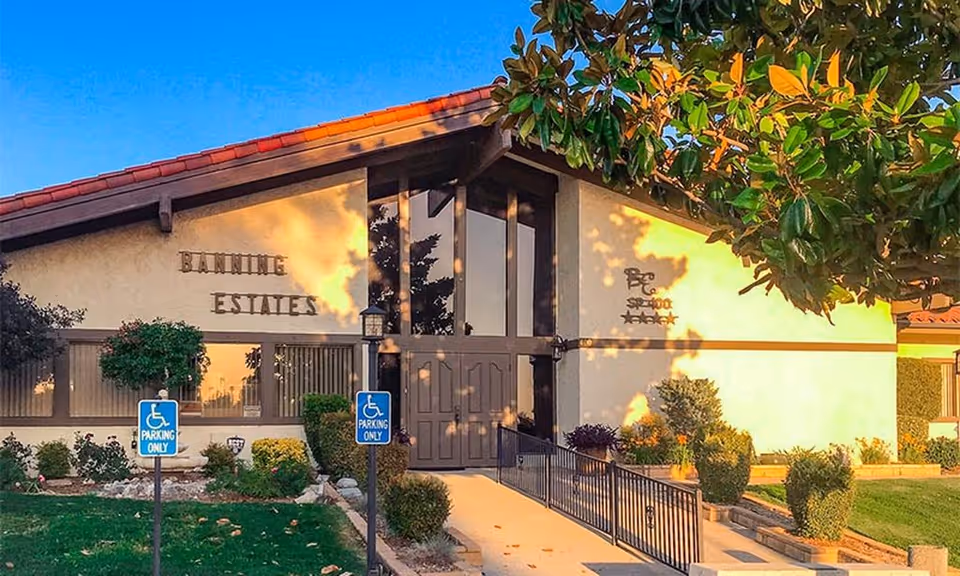 Front entrance of a one-story community building with a ramp, landscaping, and signage reading 'Banning Estates'.
